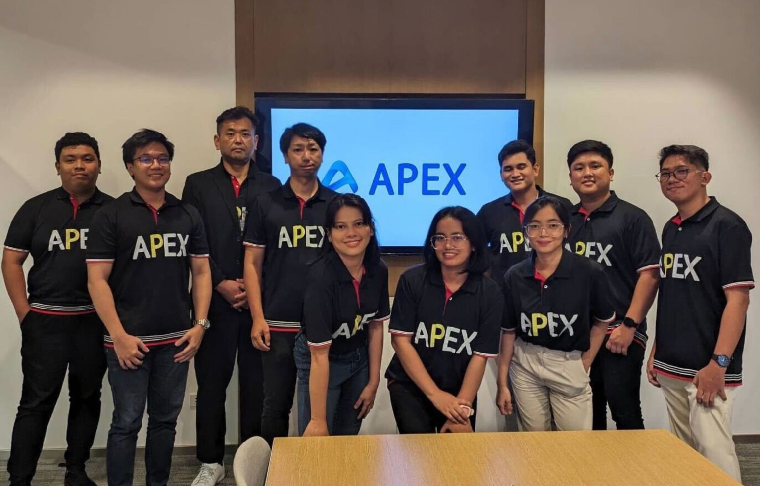 APEXのロゴの前に並ぶ、APEXのTシャツを着たメンバーたち